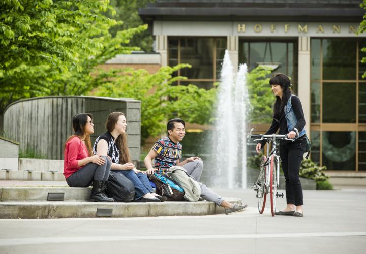 PSU Students sitting outside on campus; one student is holding a bike.